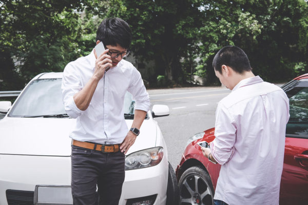 Hombres en accidente automovilístico con teléfono hablando con un seguro o policías.